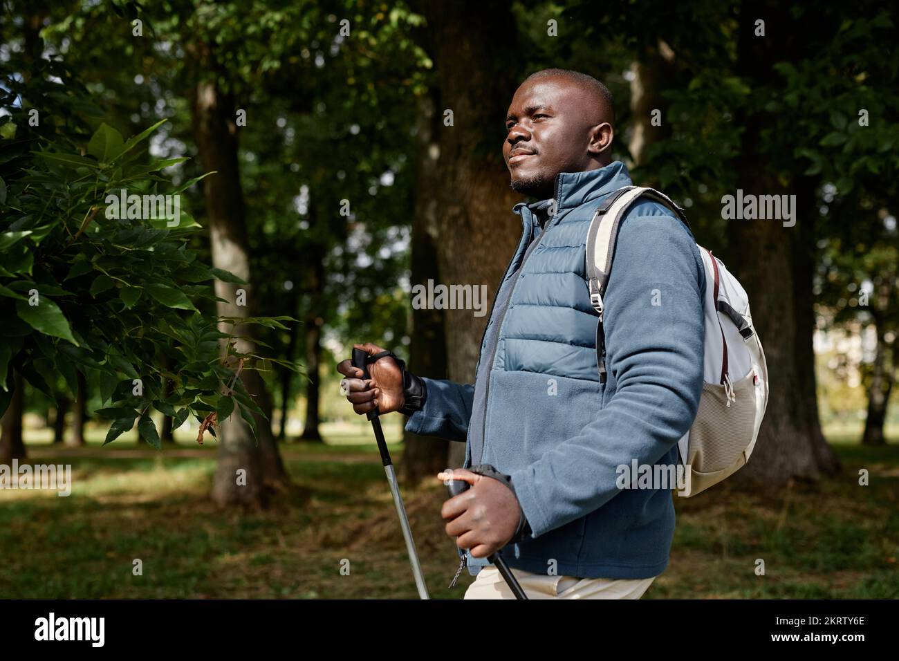 Portrait à la taille de l'homme adulte noir en randonnée avec des bâtons nordiques dans la forêt d'automne éclairée par la lumière du soleil Banque D'Images