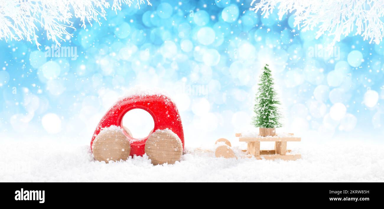 Voiture en bois rouge tirant traîneau avec Un arbre de Noël en perspective sur fond bleu vif bokeh hiver avec des branches blanches enneigées et de la neige tombant. Banque D'Images