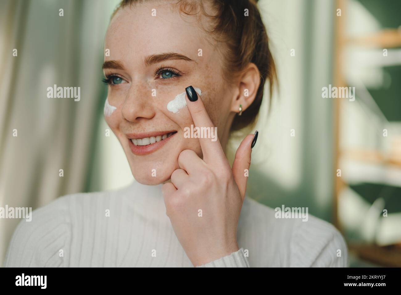 Portrait d'une femme domestique heureuse appliquant de la crème anti-âge sur le visage avec une émotion positive. Soin hydratant beauté quotidien. Banque D'Images