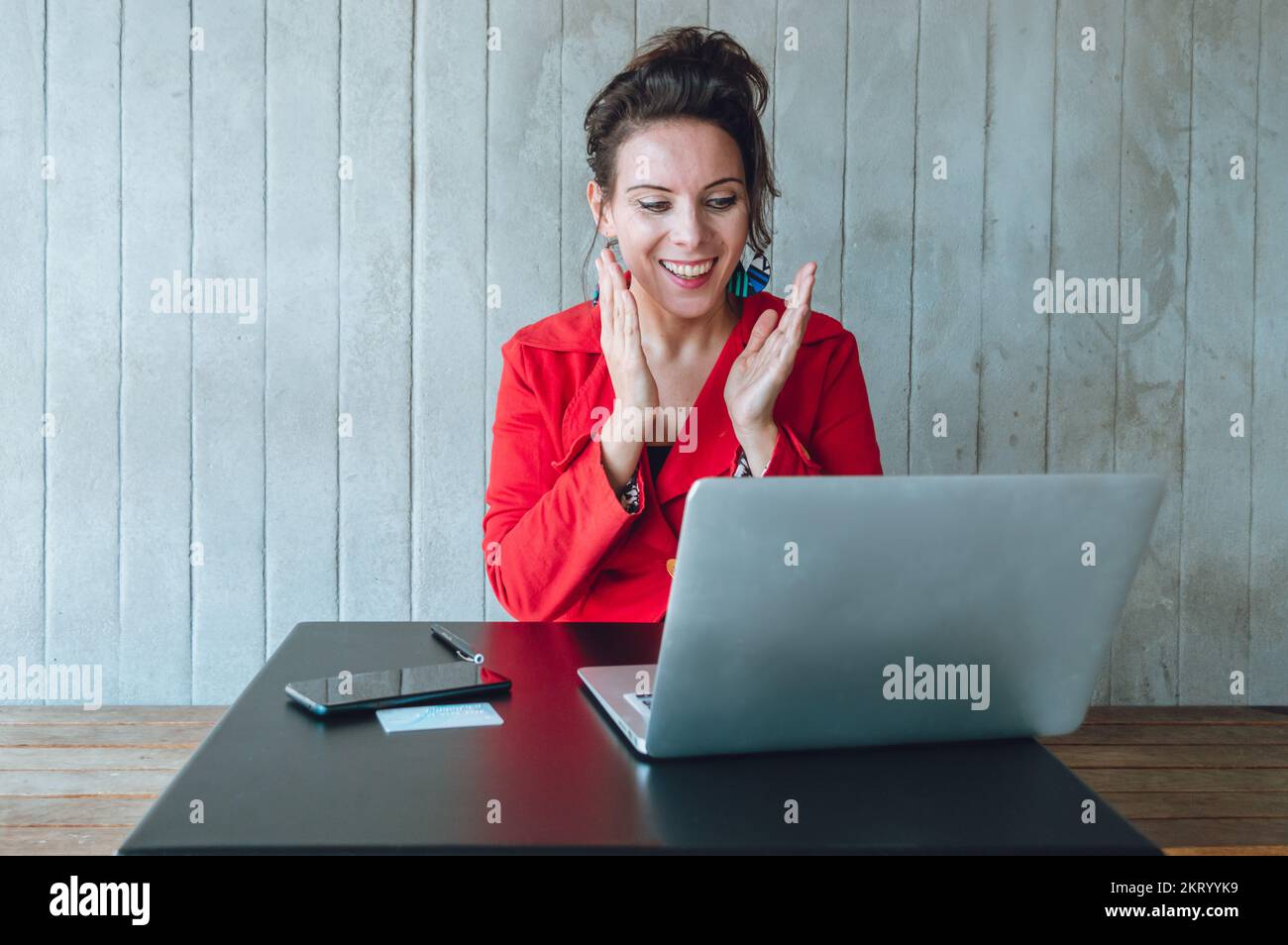 Une femme de race blanche dans un blazer rouge se réjouit de travailler avec son ordinateur portable gagnant de l'argent, assis dans un restaurant, gérant et gérant son entreprise numérique Banque D'Images