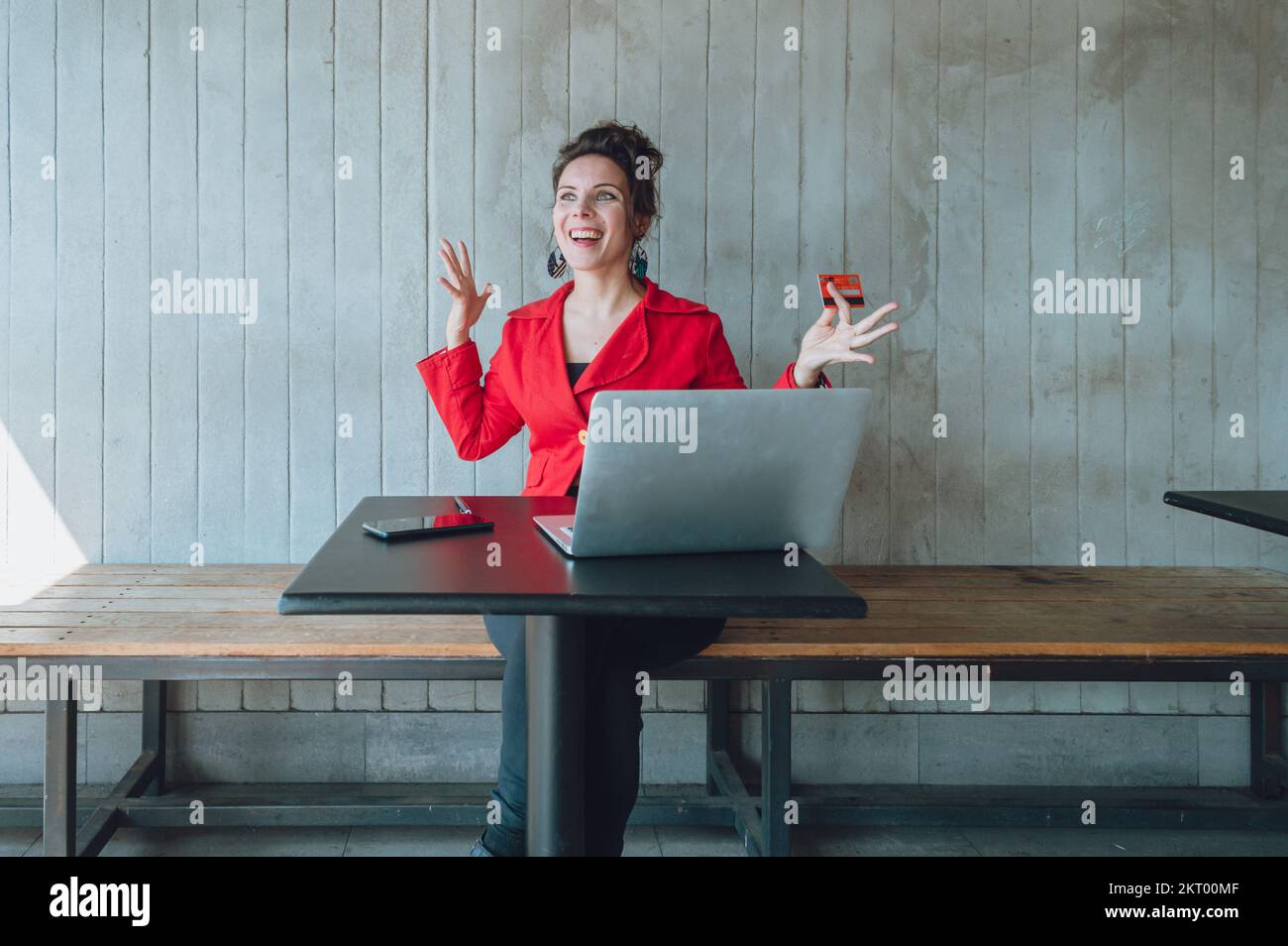 vue de face d'une femme adulte très excitée du caucase faisant des achats en ligne avec son ordinateur portable et sa carte de crédit, tout en travaillant en ligne, assis dans un restaurant. Banque D'Images