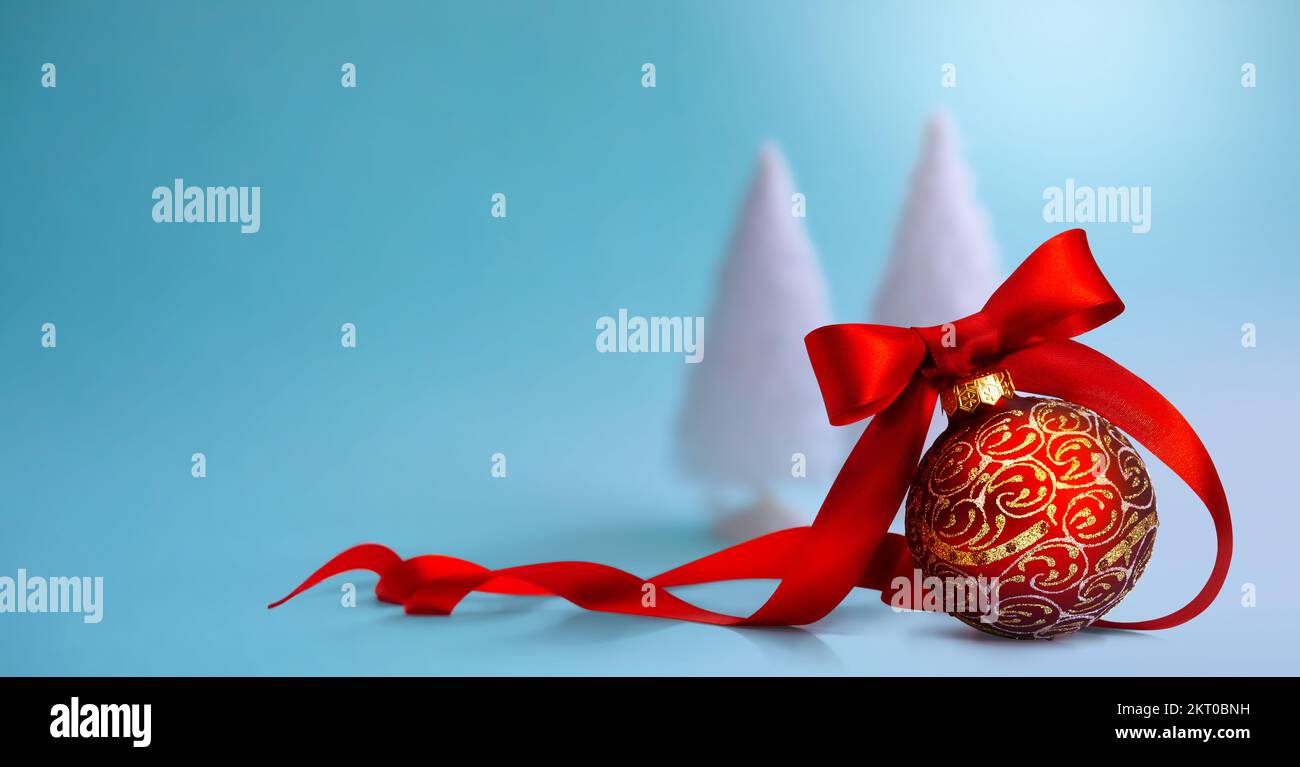 Gros plan d'une boule de Noël rouge attachée avec ruban et arbre de Noël sur une table. Bannière ou carte de vœux avec espace de copie Banque D'Images
