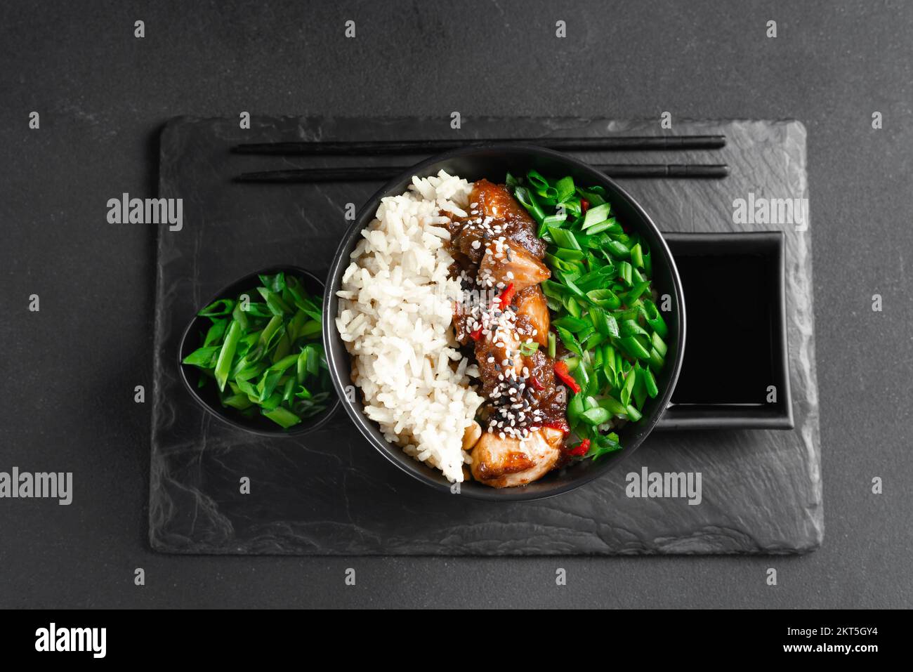 bol de riz au poulet teriyaki - cuisine asiatique. Cuisine asiatique. Cuisine thaïlandaise. Riz avec poulet et oignons verts sur fond sombre. Cuisine chinoise. Riz avec Banque D'Images