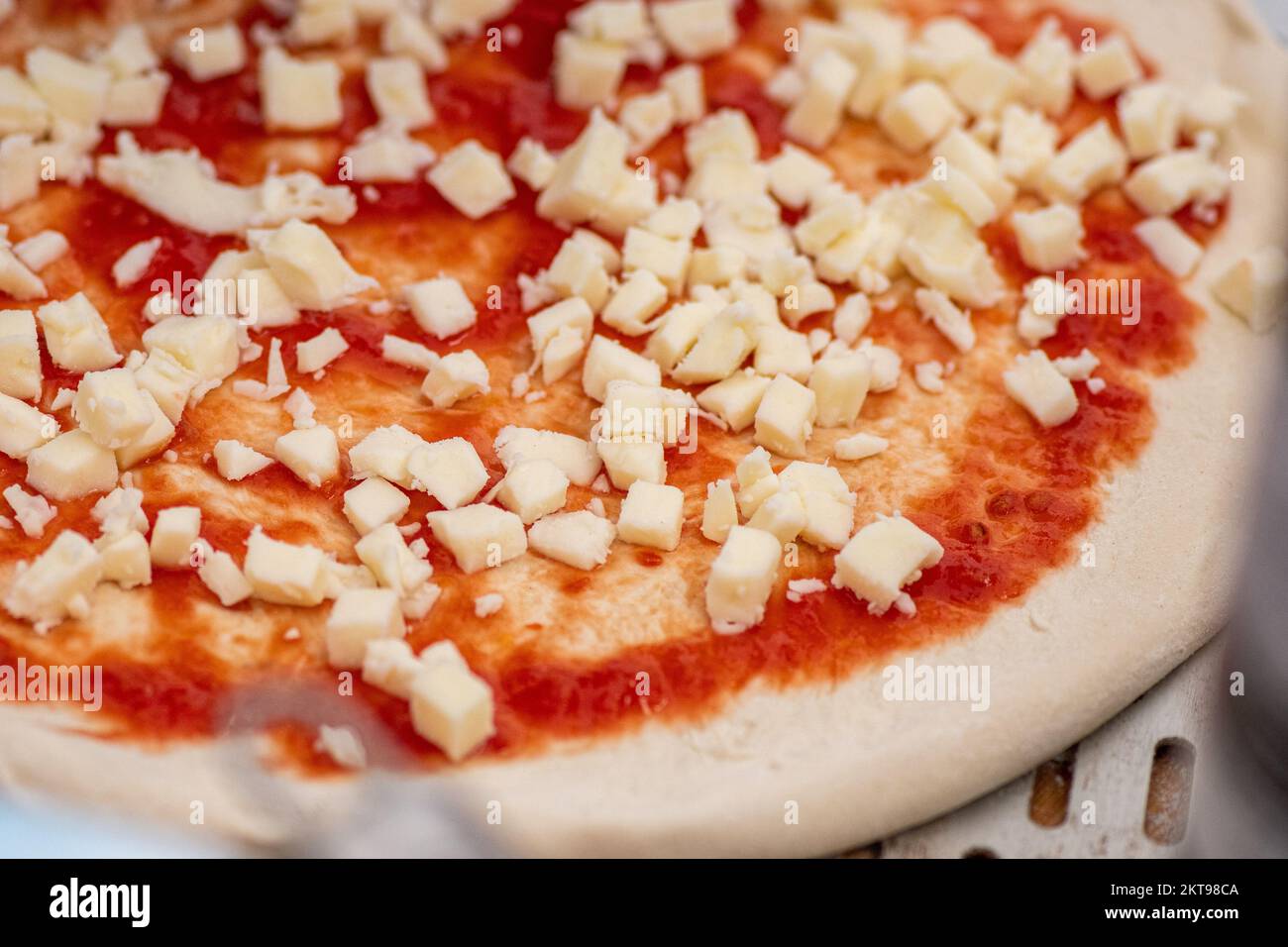 Préparer une pizza avec une sauce tomate et de la mozzarella fraîche sur une planche de bois avec des ingrédients et des outils autour, gros plan Banque D'Images