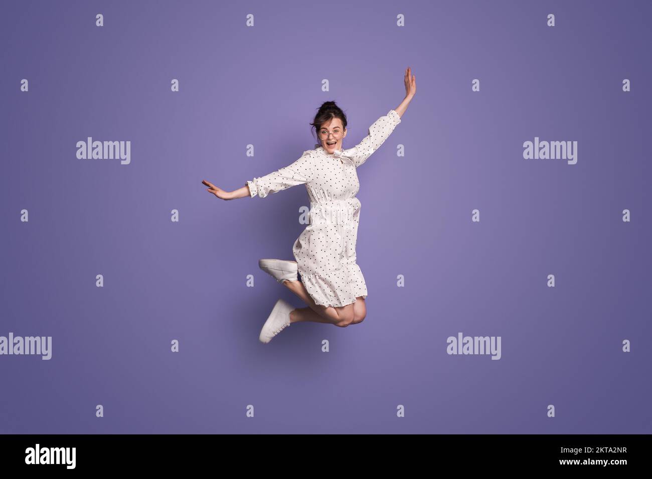 Photo de la taille du corps de la jolie fille qui se porte en robe tout en sautant isolé sur fond violet. Des gens heureux émotions positives Banque D'Images