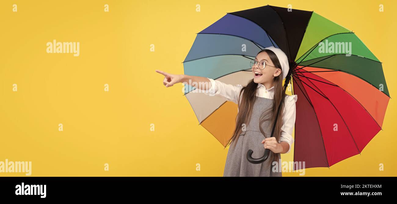 bonne fille de l'adolescence sous parapluie coloré en automne pointant le doigt sur l'espace de copie, la publicité. Enfant avec parapluie d'automne, temps pluvieux, horizontal Banque D'Images
