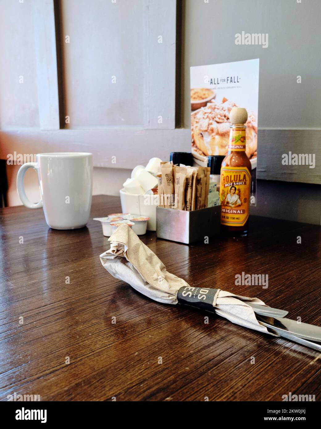 Table de restaurant petit-déjeuner avec ustensiles emballés, tasse de café et condiments. Banque D'Images