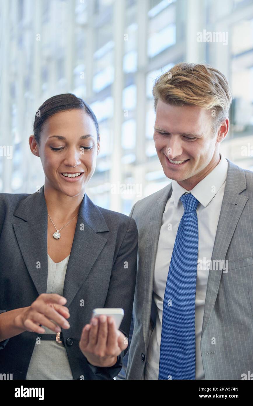 Applications qui aident les entreprises à optimiser leurs ventes. deux collègues professionnels se tenant debout et regardant quelque chose sur un téléphone mobile. Banque D'Images