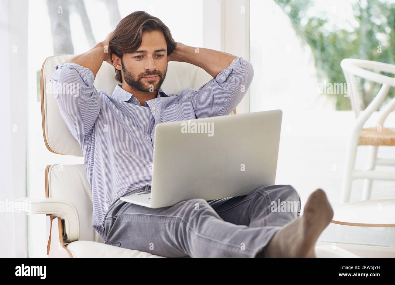 Mélange affaires et loisirs.Un homme d'affaires charmant se détendant tout en travaillant sur son ordinateur portable. Banque D'Images