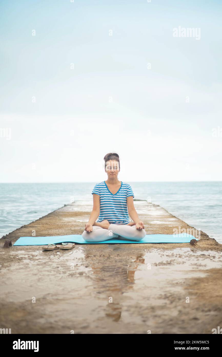 Femme instructeur de yoga assis dans la posture de lotus mains mudra en admirant le paysage de la côte de mer Banque D'Images