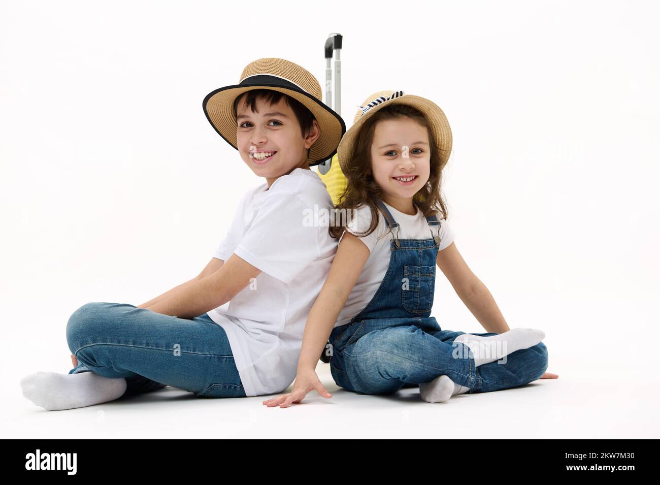 Adorables enfants, garçon et fille assis avec leur dos à l'autre cutely sourire sur l'appareil photo, isolé sur fond blanc Banque D'Images