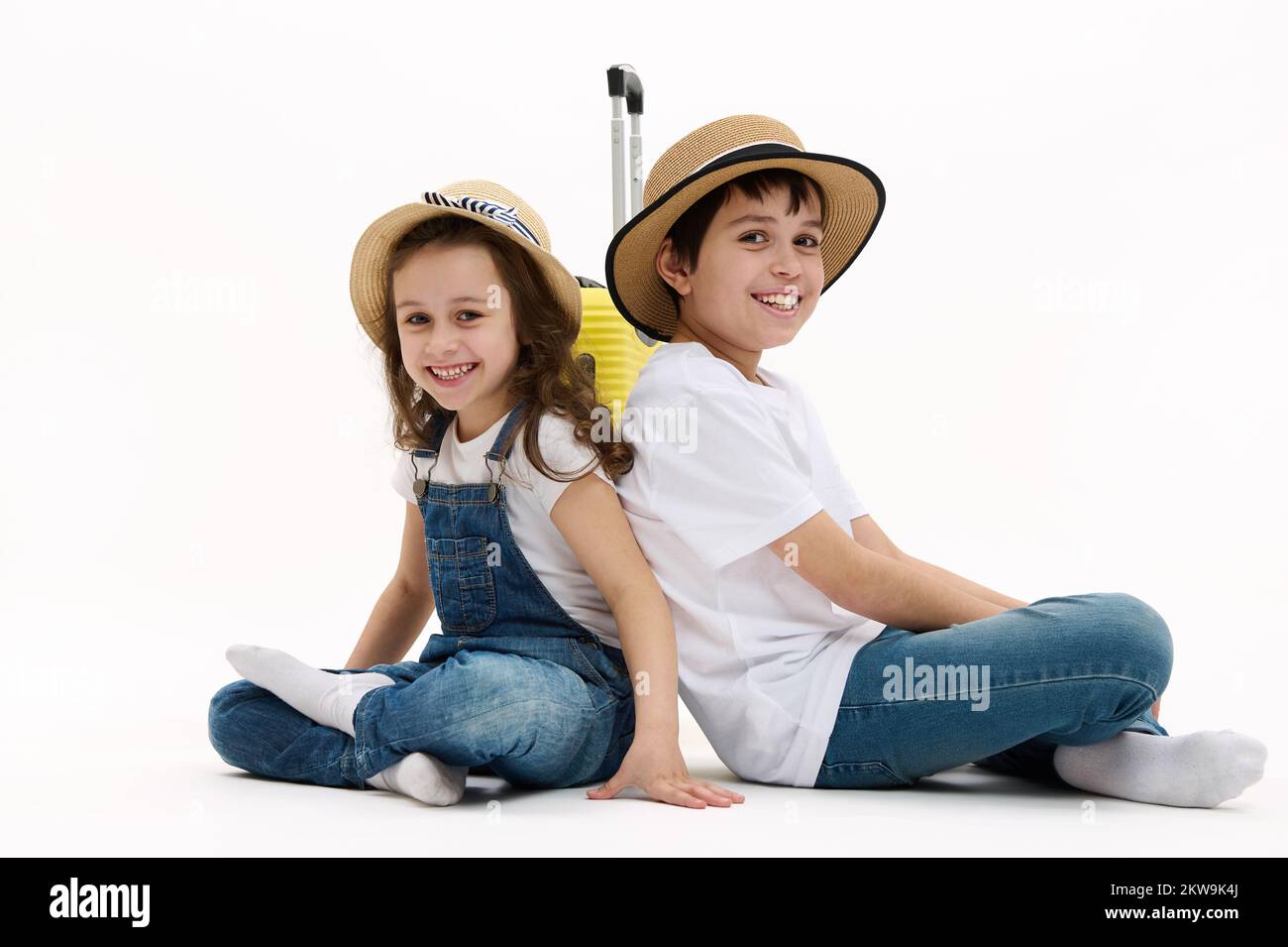 Les enfants adorables, frère et sœur s'assoient avec leur dos les uns aux autres dans la posture du lotus, sourient sur l'appareil photo, sur fond blanc Banque D'Images
