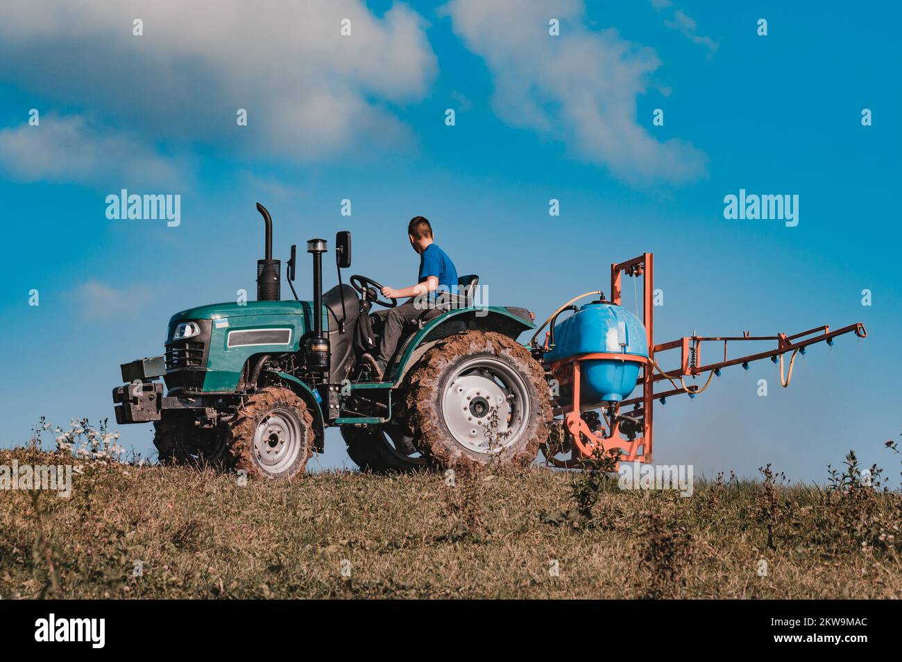 Un petit tracteur sur le fond du ciel cultive le champ avant le labour, le processus de pulvérisation des champs avec des herbicides, travail d'automne en t Banque D'Images