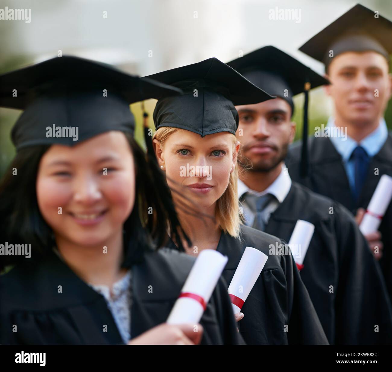 Il est payant d'étudier. Un groupe de diplômés de collège debout en chapeau et en robe et portant leurs diplômes. Banque D'Images