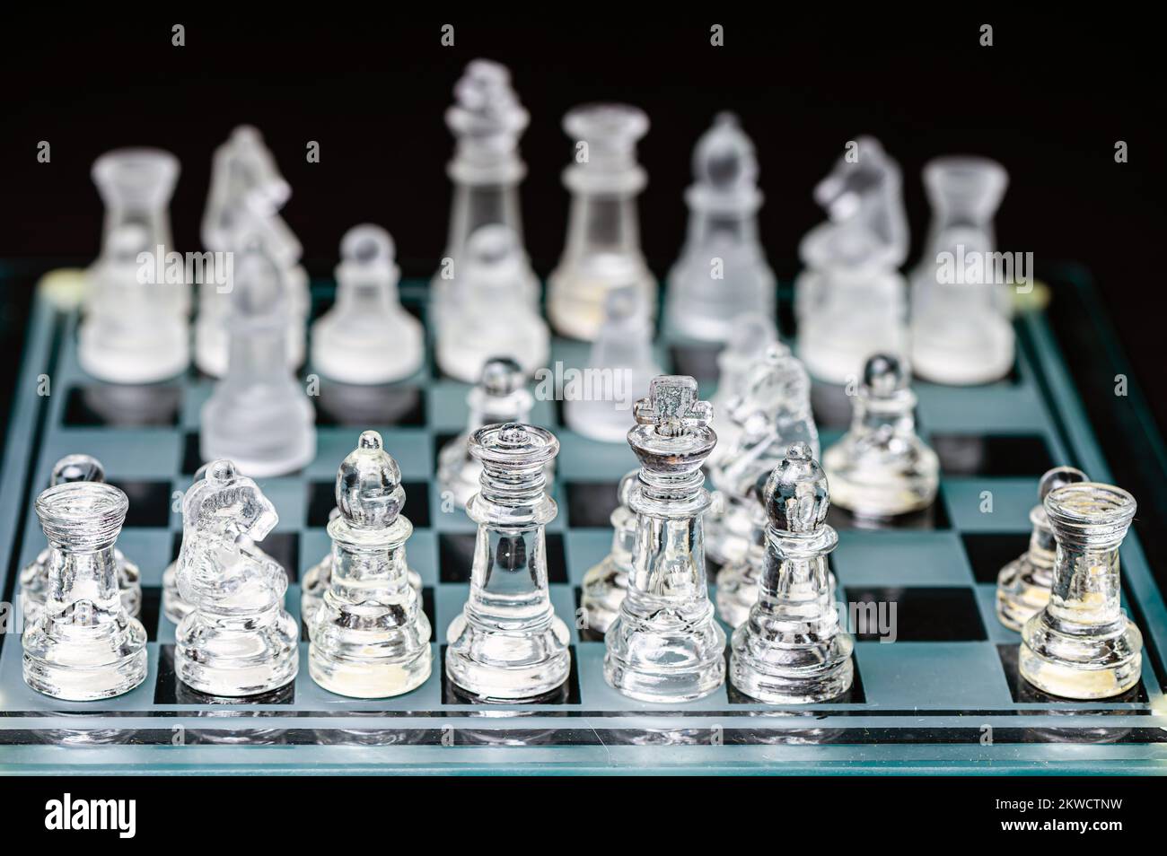 verre transparent, pièces d'échecs transparentes sur un damier, mise au point sélective, gros plan, isolé sur le noir Banque D'Images