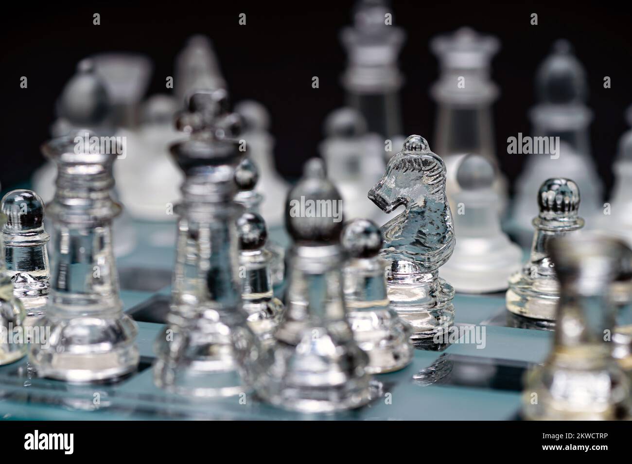verre transparent, pièces d'échecs transparentes sur un damier, mise au point sélective, gros plan, isolé sur le noir Banque D'Images