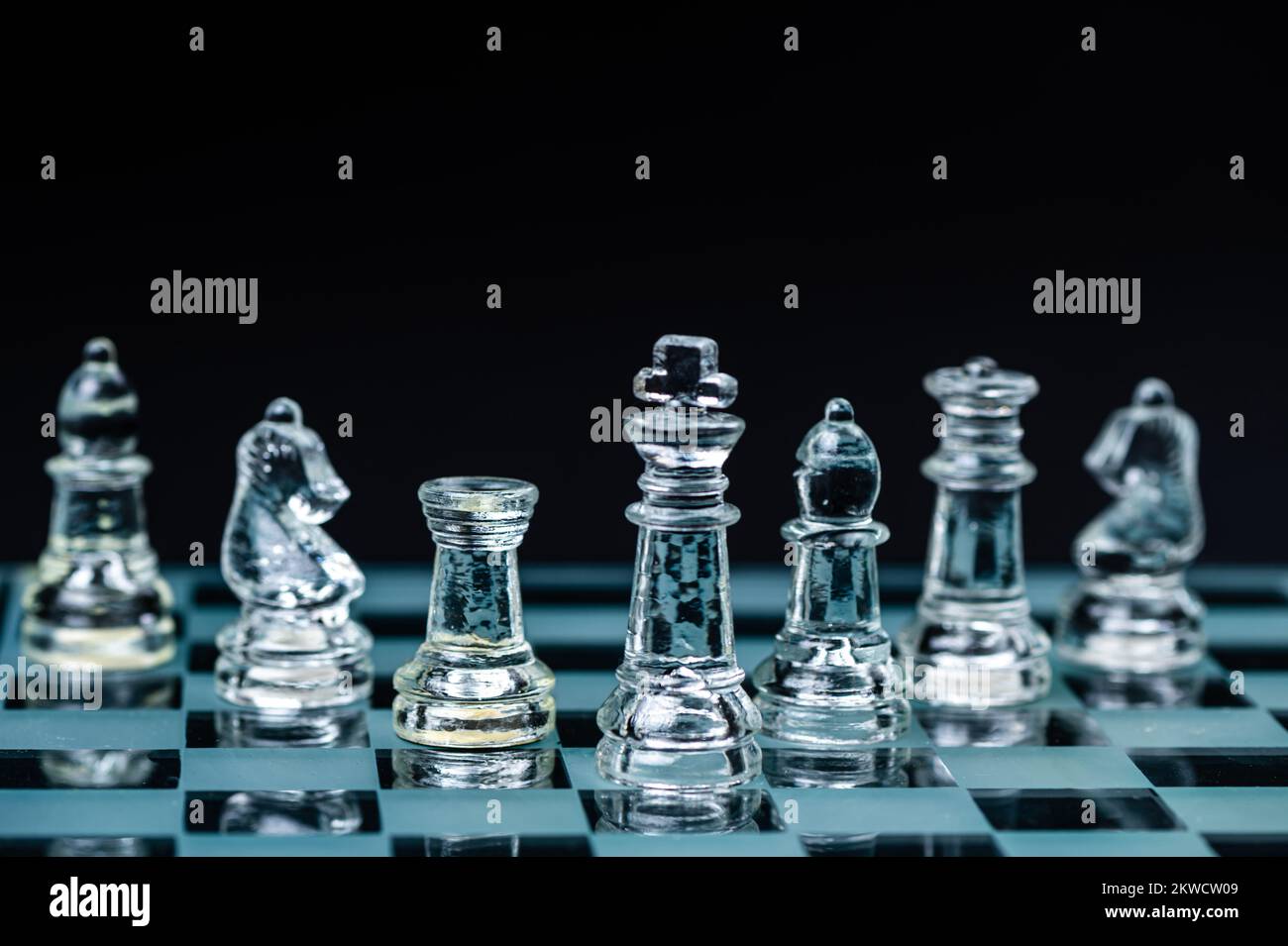 personnages d'échecs en verre transparent disposés en rangée et reflétant dans un échiquier en verre. Isolé sur le noir Banque D'Images