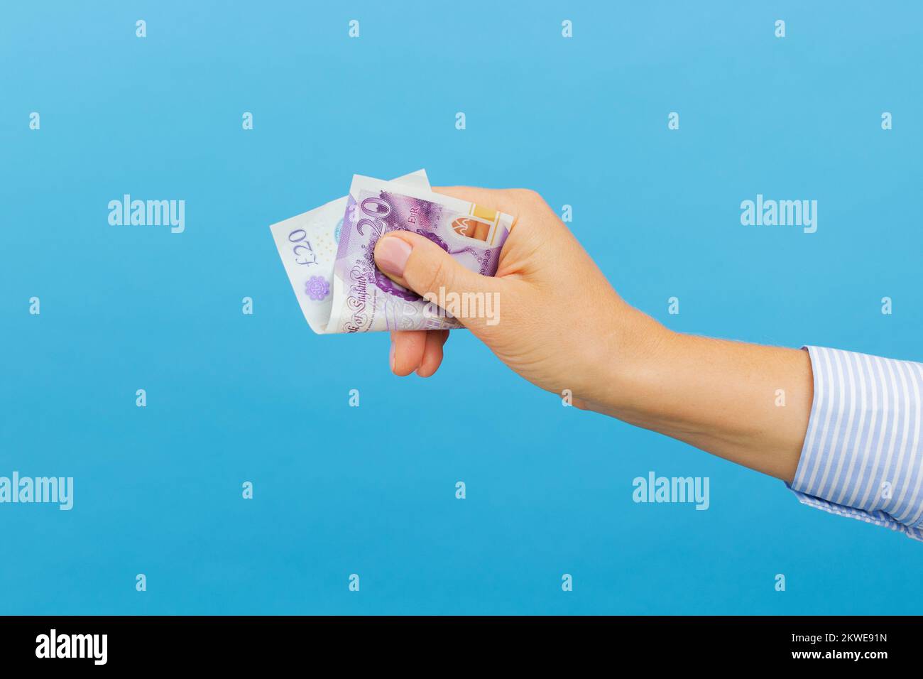 Main de femme tenant vingt livres sterling billet de banque isolé sur fond bleu. Livres sterling argent, billets de banque en espèces Banque D'Images
