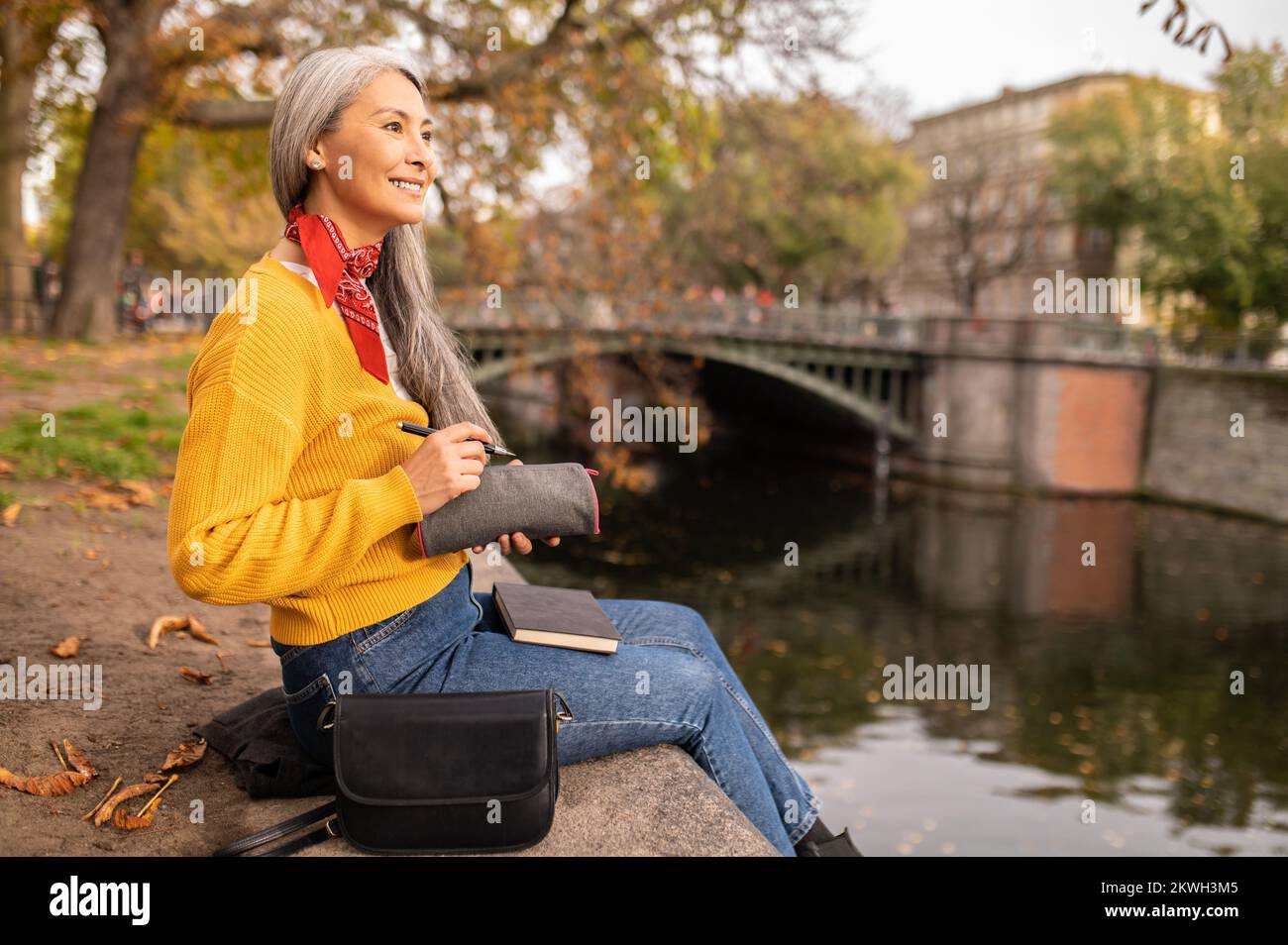 Femme assise sur la rive de la rivière et prenant des notes Banque D'Images