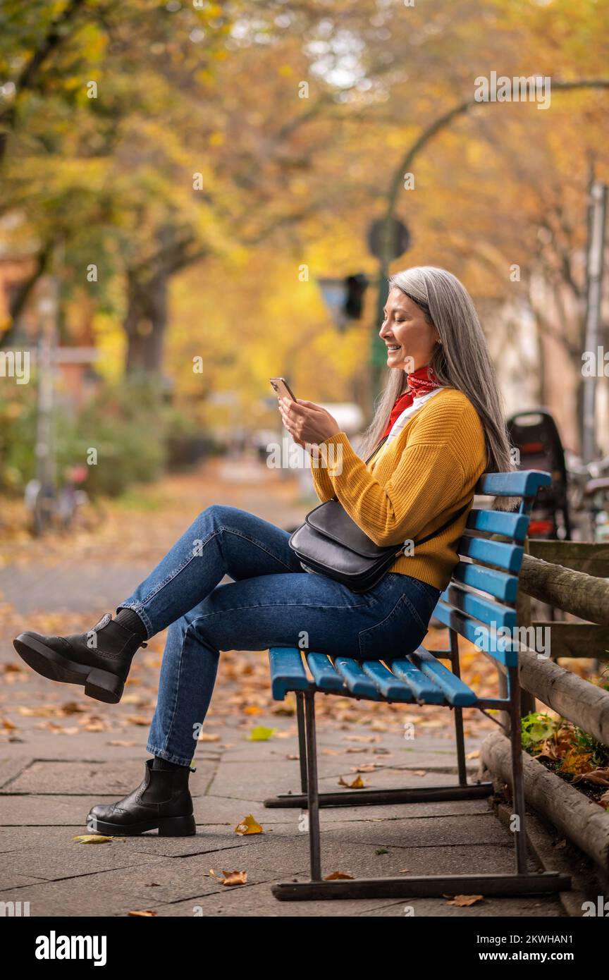 Une bonne femme assise sur le banc et parlant au téléphone Banque D'Images