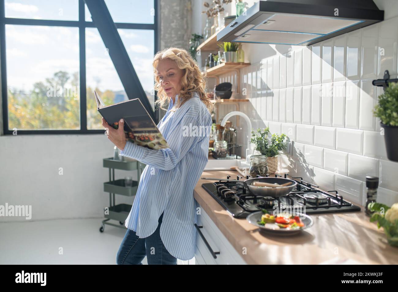 Une femme blonde lit une réceptionniste dans un livre de cuisine Banque D'Images