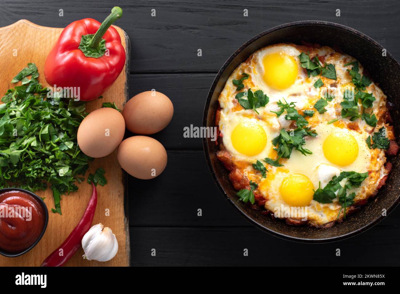 Shakshuka dans une poêle à repasser avec ingrédients. Plat traditionnel du Moyen-Orient. Œufs frits avec tomates, poivrons, légumes et herbes Banque D'Images