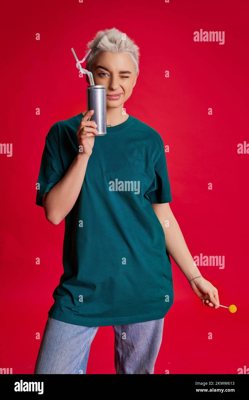 Portrait d'une jeune femme élégante avec des cheveux courts posant dans des vêtements  comfortabel décontractés, buvant du coke isolé sur fond rouge Photo Stock -  Alamy