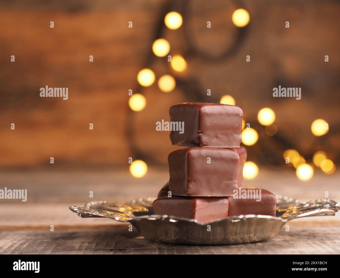 Dés de chocolat empilés sur une plaque argentée sur une table en bois avec des lumières de Noël Banque D'Images