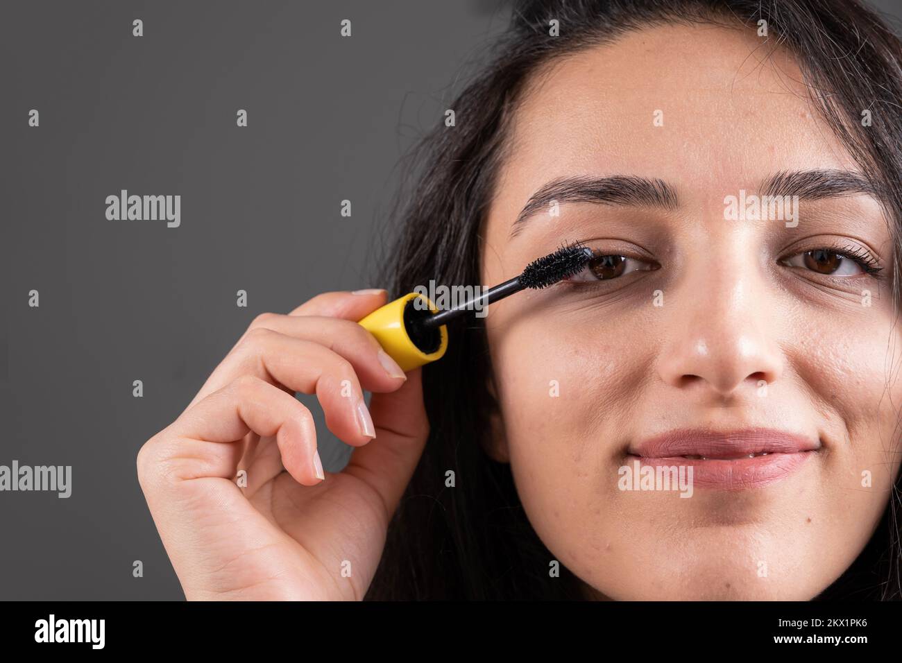 En utilisant la mascara, belle femme caucasienne en utilisant la mascara sur les cils. Concept de maquillage frontal court en gros plan. Jeune fille heureuse aux cheveux bruns. Banque D'Images