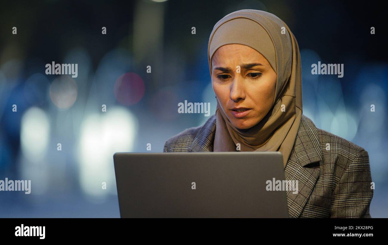 Portrait d'une femme d'affaires musulmane dans hijab se trouve dans la ville en plein air le soir travaillant avec un ordinateur portable inquiétude au sujet du problème de regarder des gains d'ordinateur dit Banque D'Images