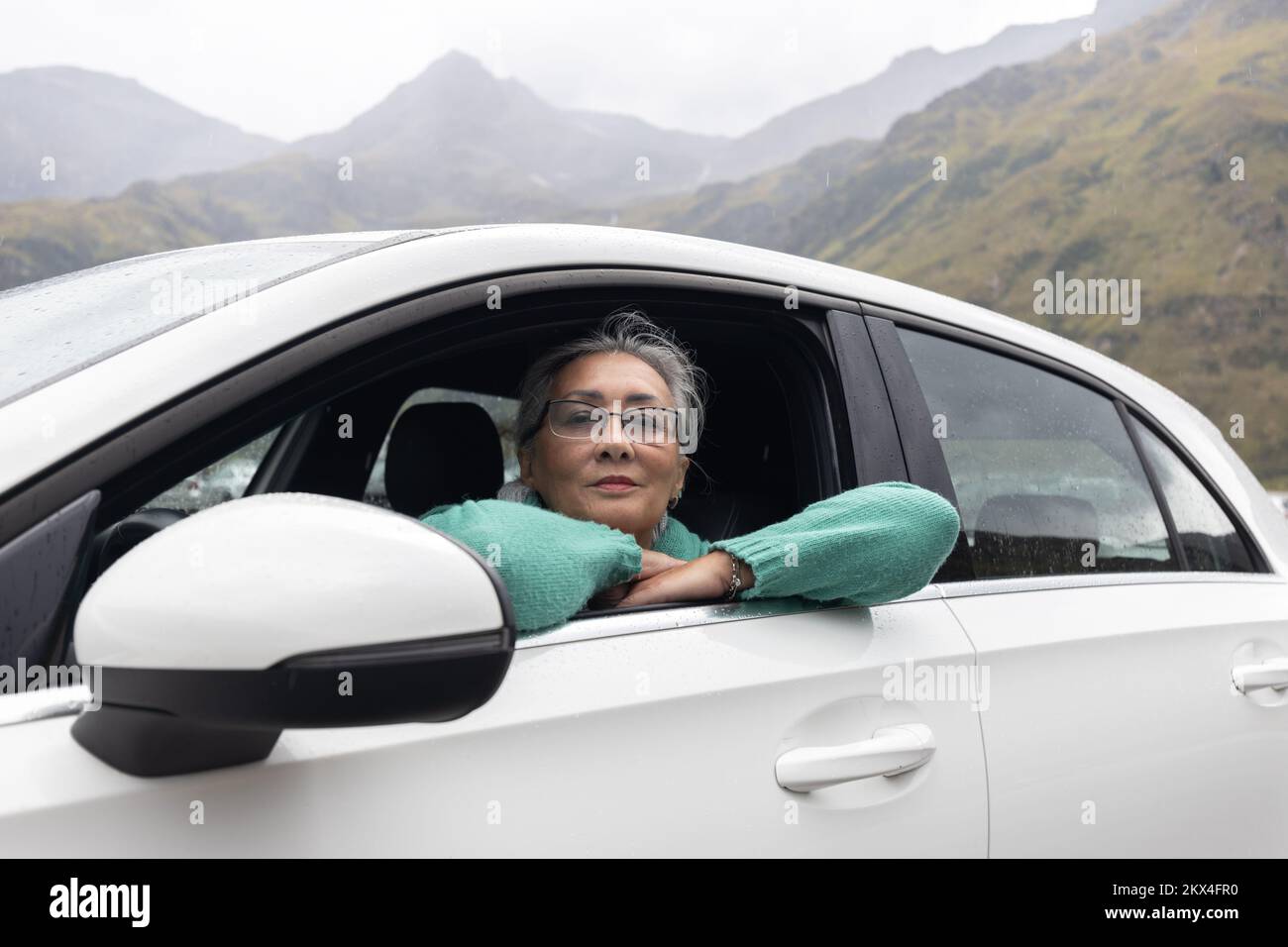 Une femme aux cheveux gris dans une voiture dans le siège du conducteur sur fond de montagnes alpines Banque D'Images