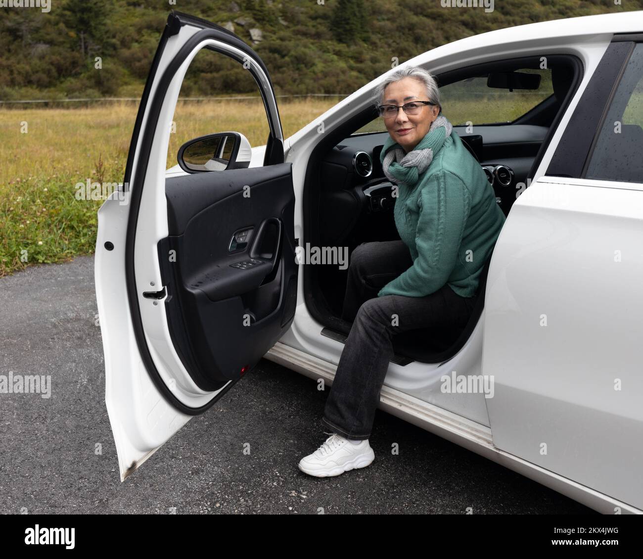 Une femme aux cheveux gris sort d'une voiture et sourit à la caméra Banque D'Images