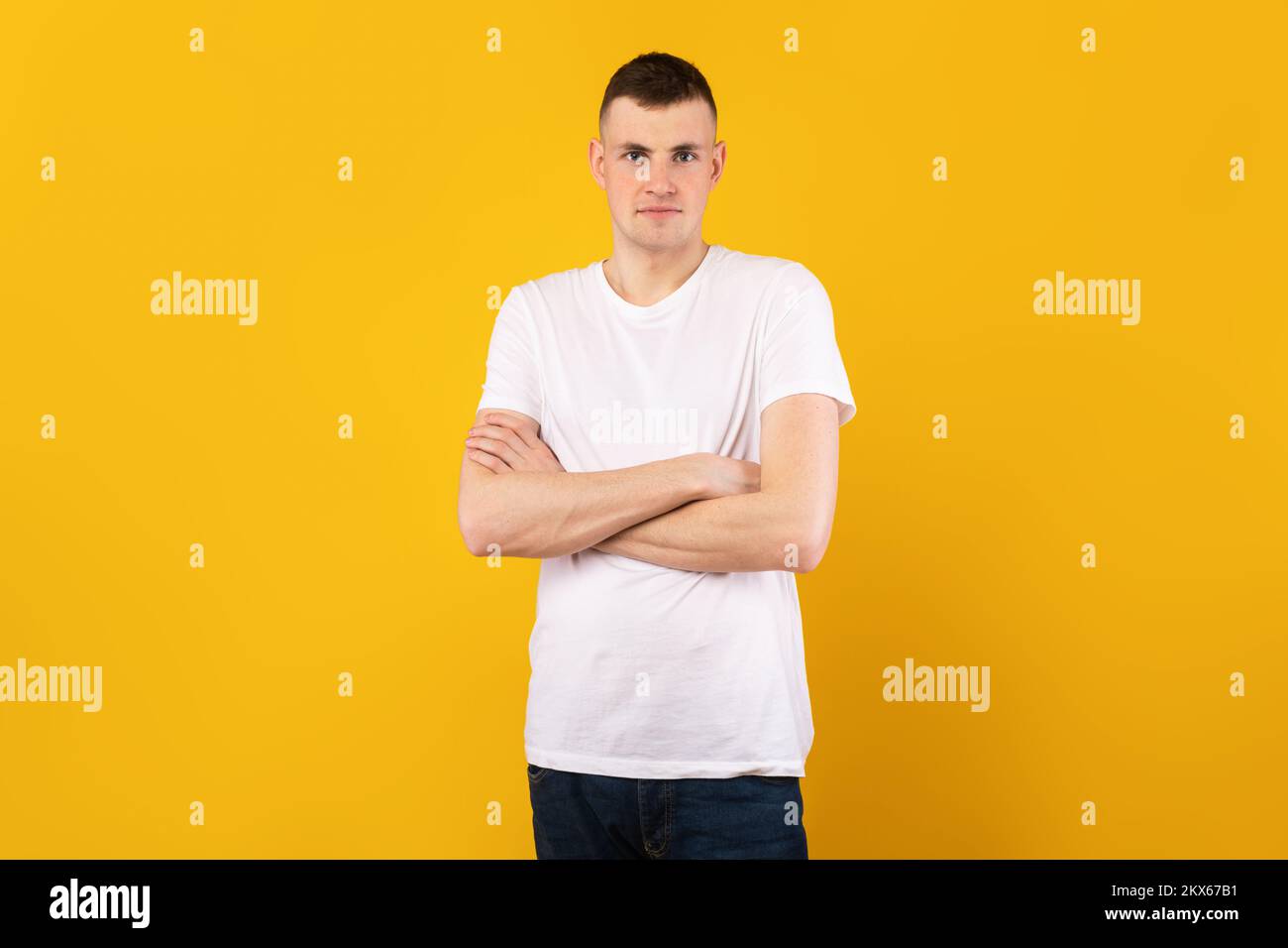 Portrait masculin. Beau type caucasien avec bras pliés regardant la caméra, portant un t-shirt, posant sur fond jaune Banque D'Images