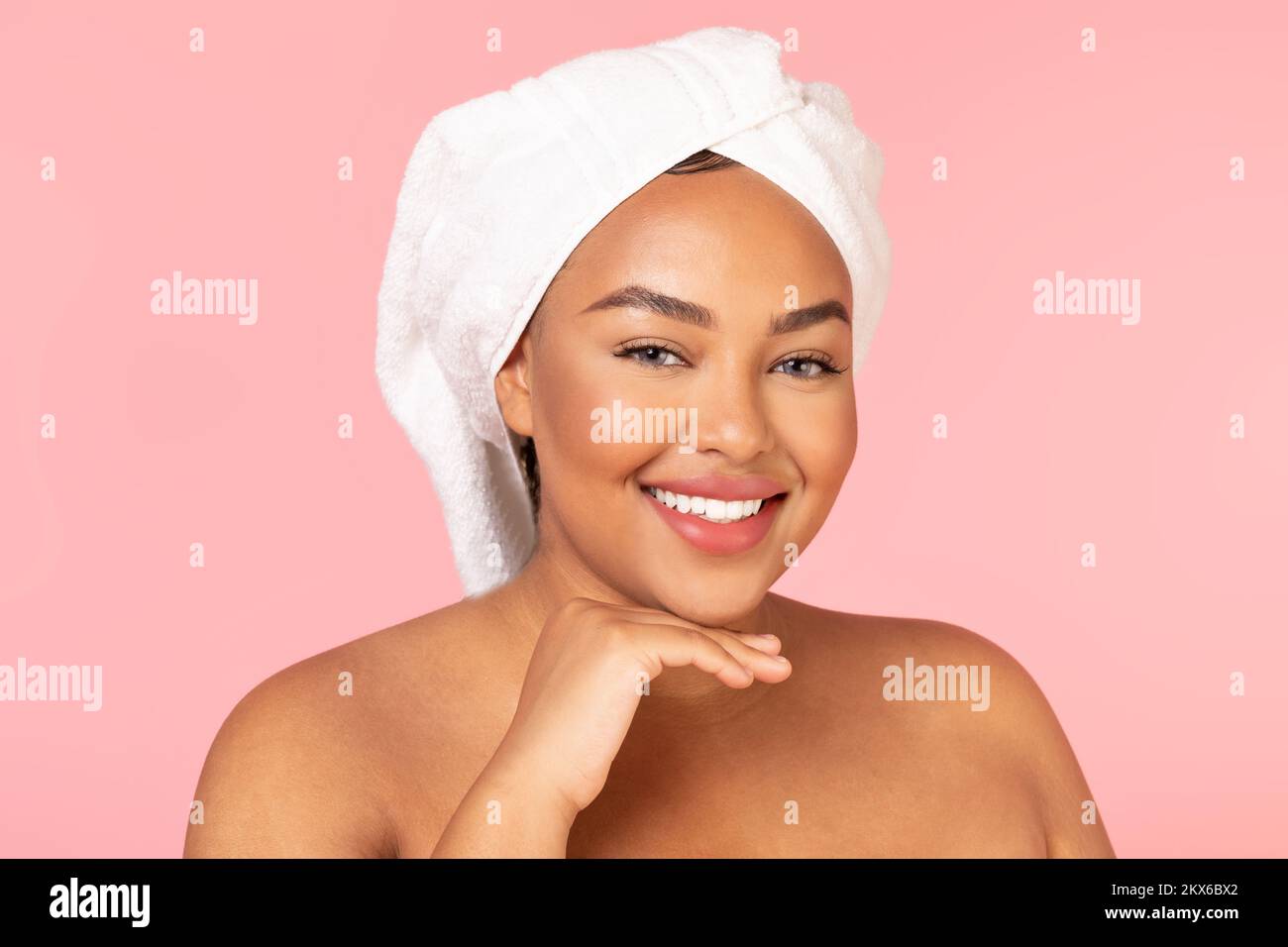 Concept après spa. Portrait d'une femme noire chubby avec serviette de bain sur la tête et peau brillante parfaite souriant à l'appareil photo Banque D'Images