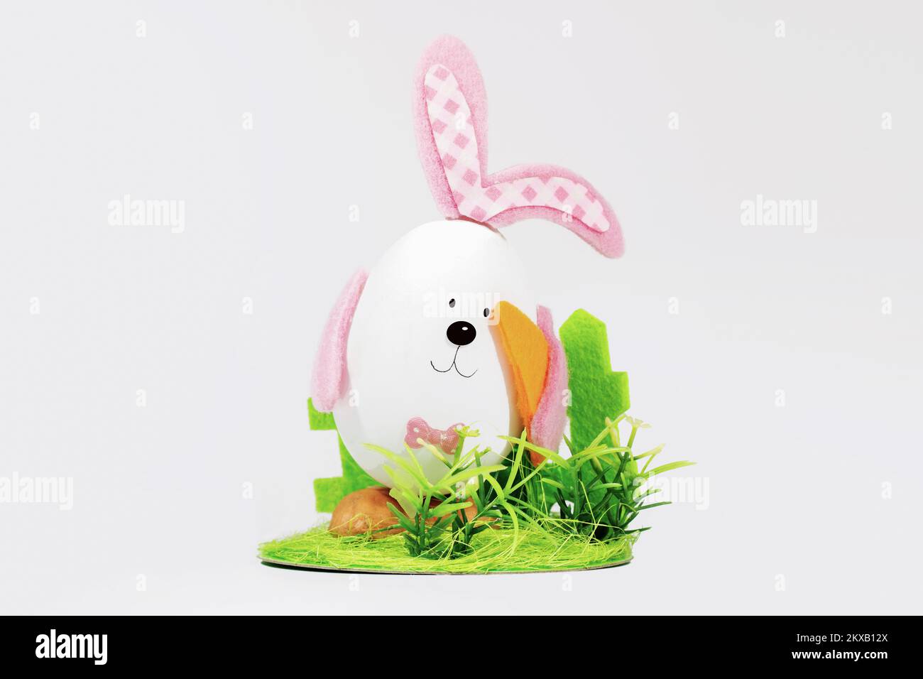 Oeuf de Pâques avec des oreilles sous forme de lapin de Pâques, avec des carottes sur une pelouse verte. Carte de Pâques. Concept de pâques minimal Banque D'Images