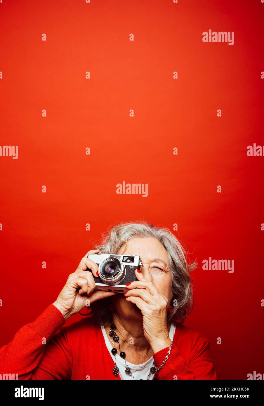 Femme âgée vêtue de vêtements rouges, prenant des photos avec un ancien appareil photo, sur fond rouge Banque D'Images Femme âgée vêtue de vêtements rouges, prenant des photos avec un ancien appareil photo, sur fond rouge Banque D'Images