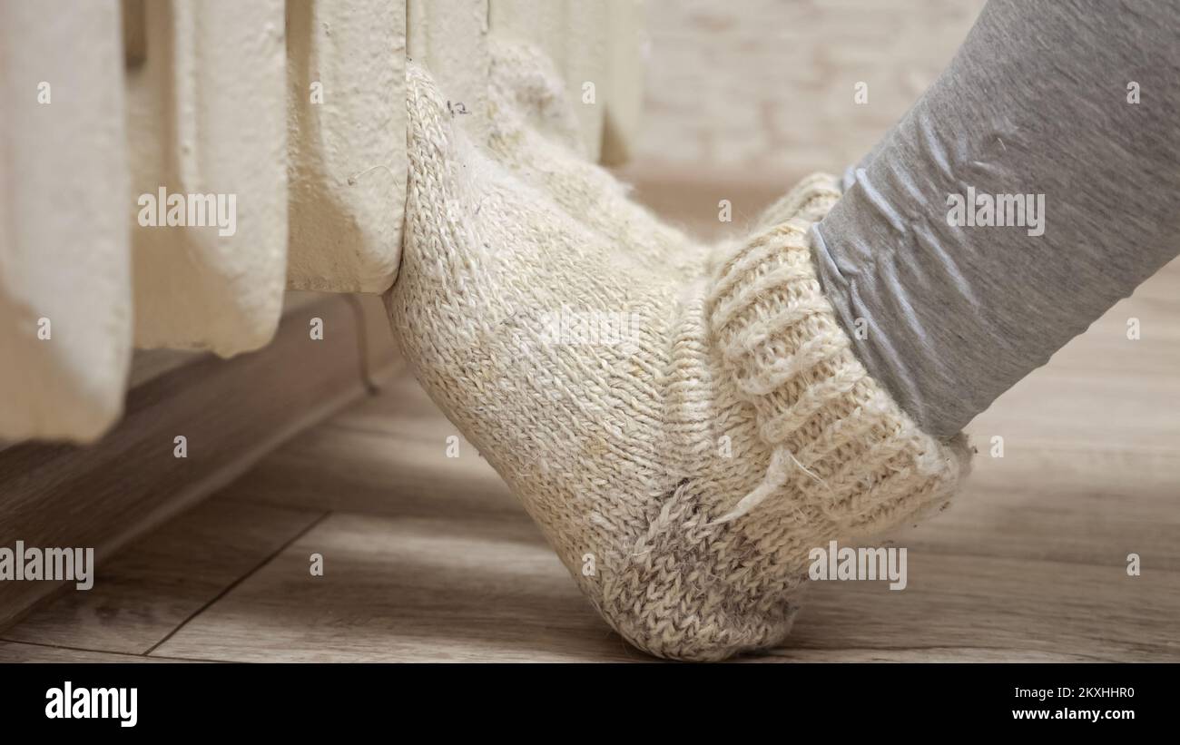 La femme met les jambes dans des chaussettes chaudes en laine sur le radiateur de chauffage central de la salle. Banque D'Images