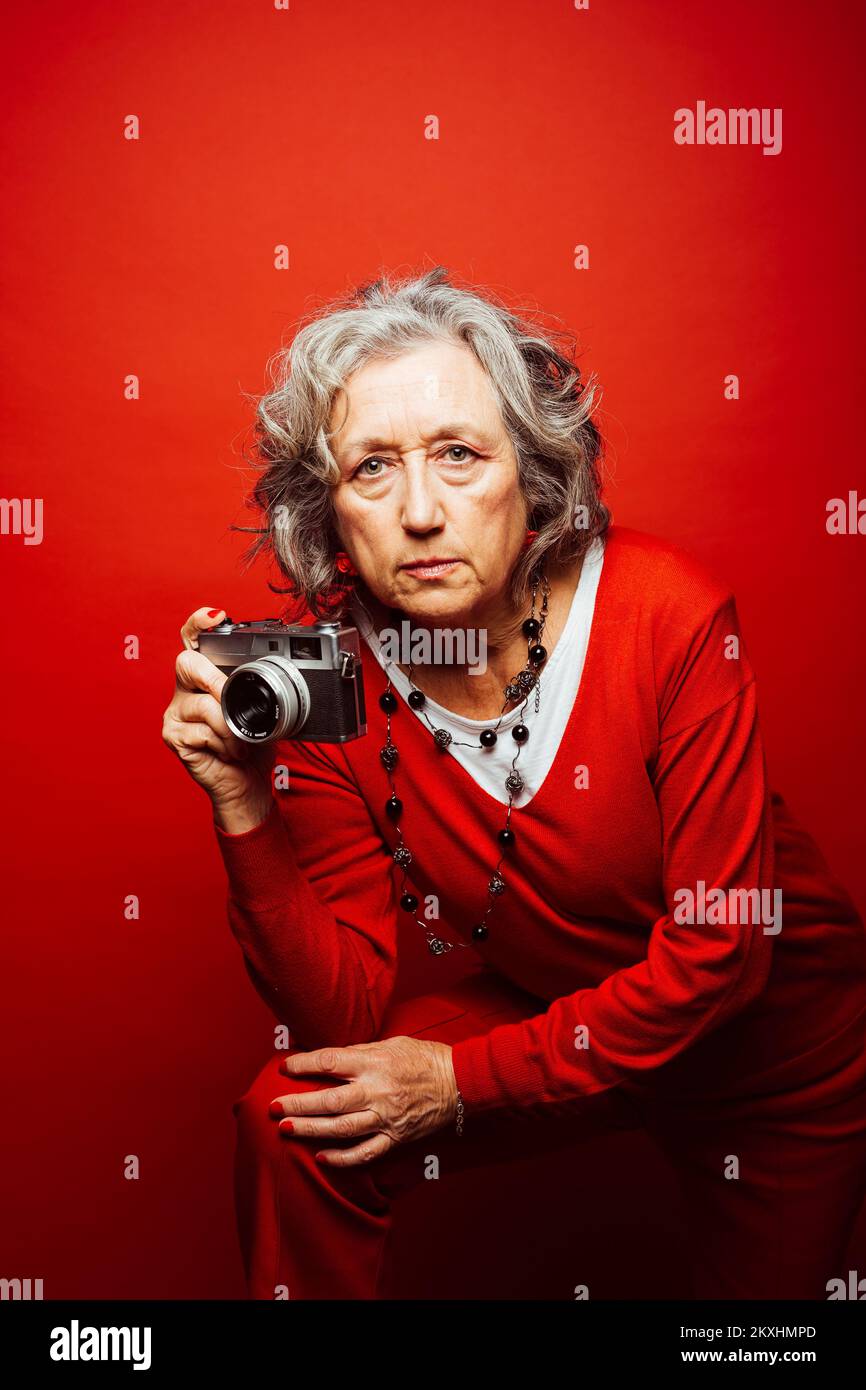 Femme âgée vêtue de vêtements rouges, prenant des photos avec un ancien appareil photo, sur fond rouge Banque D'Images Femme âgée vêtue de vêtements rouges, prenant des photos avec un ancien appareil photo, sur fond rouge Banque D'Images