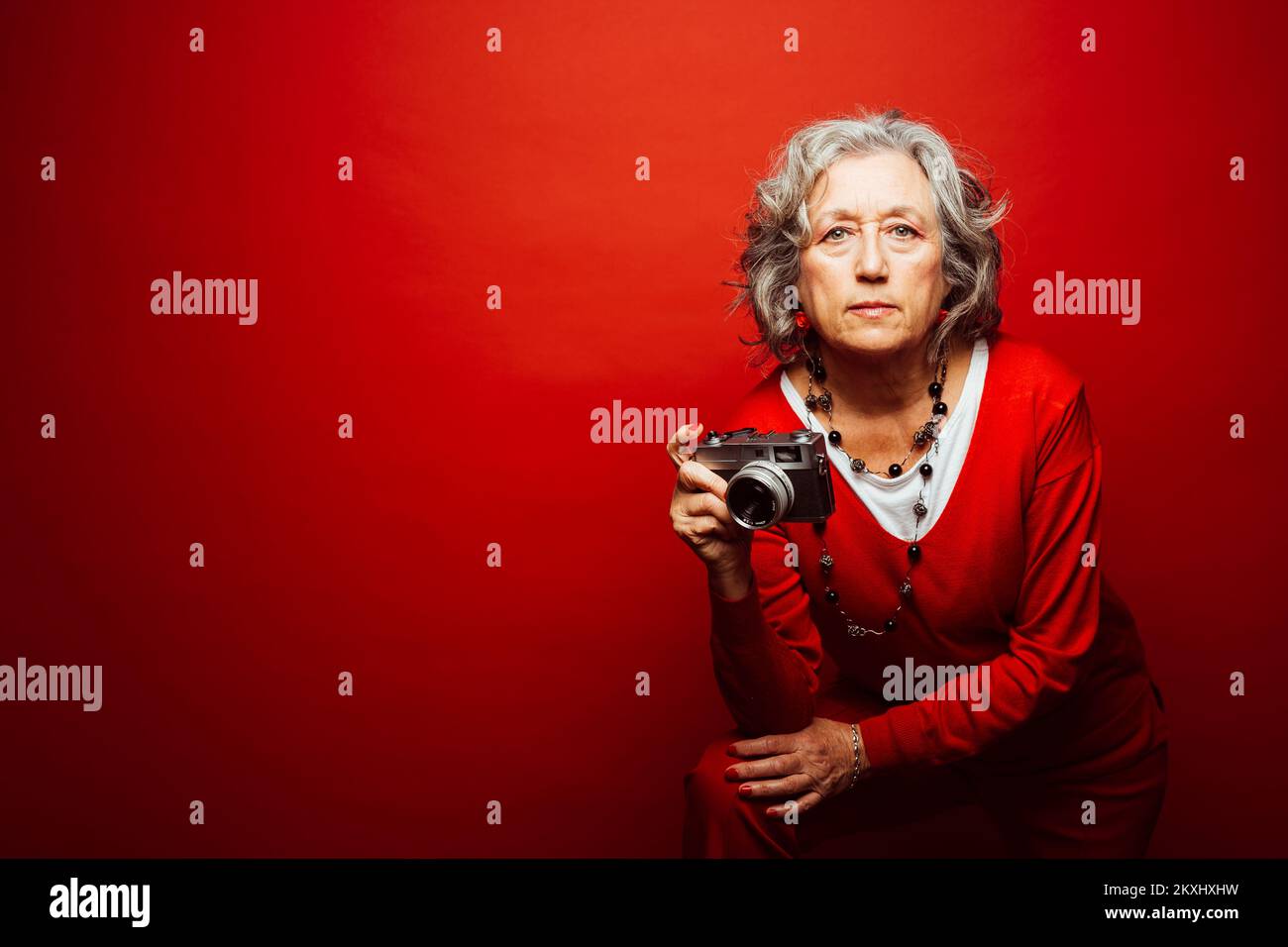 Femme âgée vêtue de vêtements rouges, prenant des photos avec un ancien appareil photo, sur fond rouge Banque D'Images