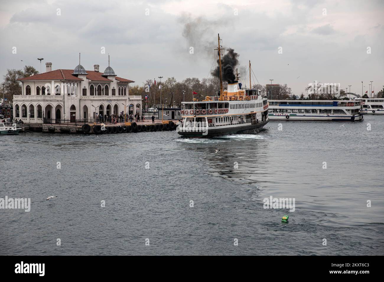 Un ferry de la ville s'approche de l'embarcadère tout en émettant de la fumée pendant une journée nuageux à Istanbul. Banque D'Images