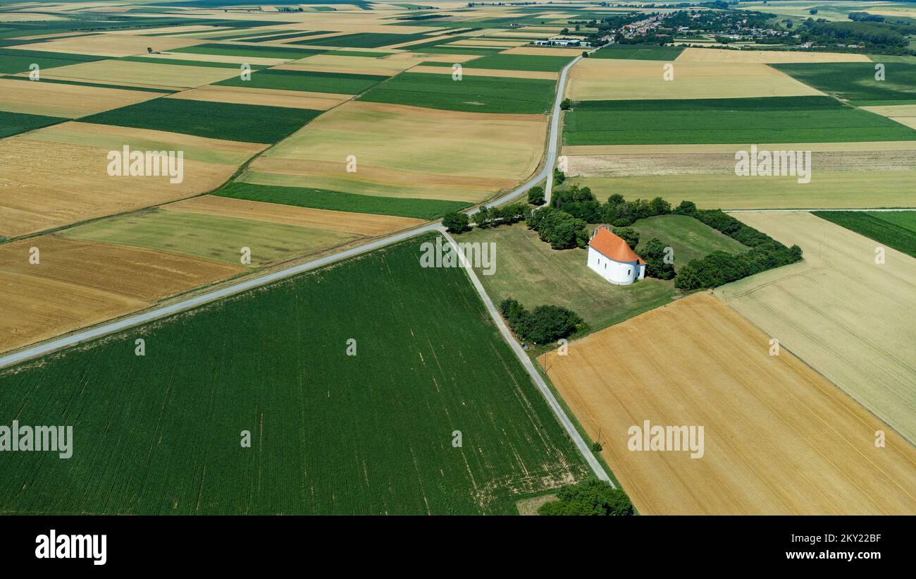 Vue aérienne de grandes terres agricoles cultivées et de l'église Saint-Pierre et Paul près de Topolje à Baranja, Croatie sur 15 juin 2022. Banque D'Images