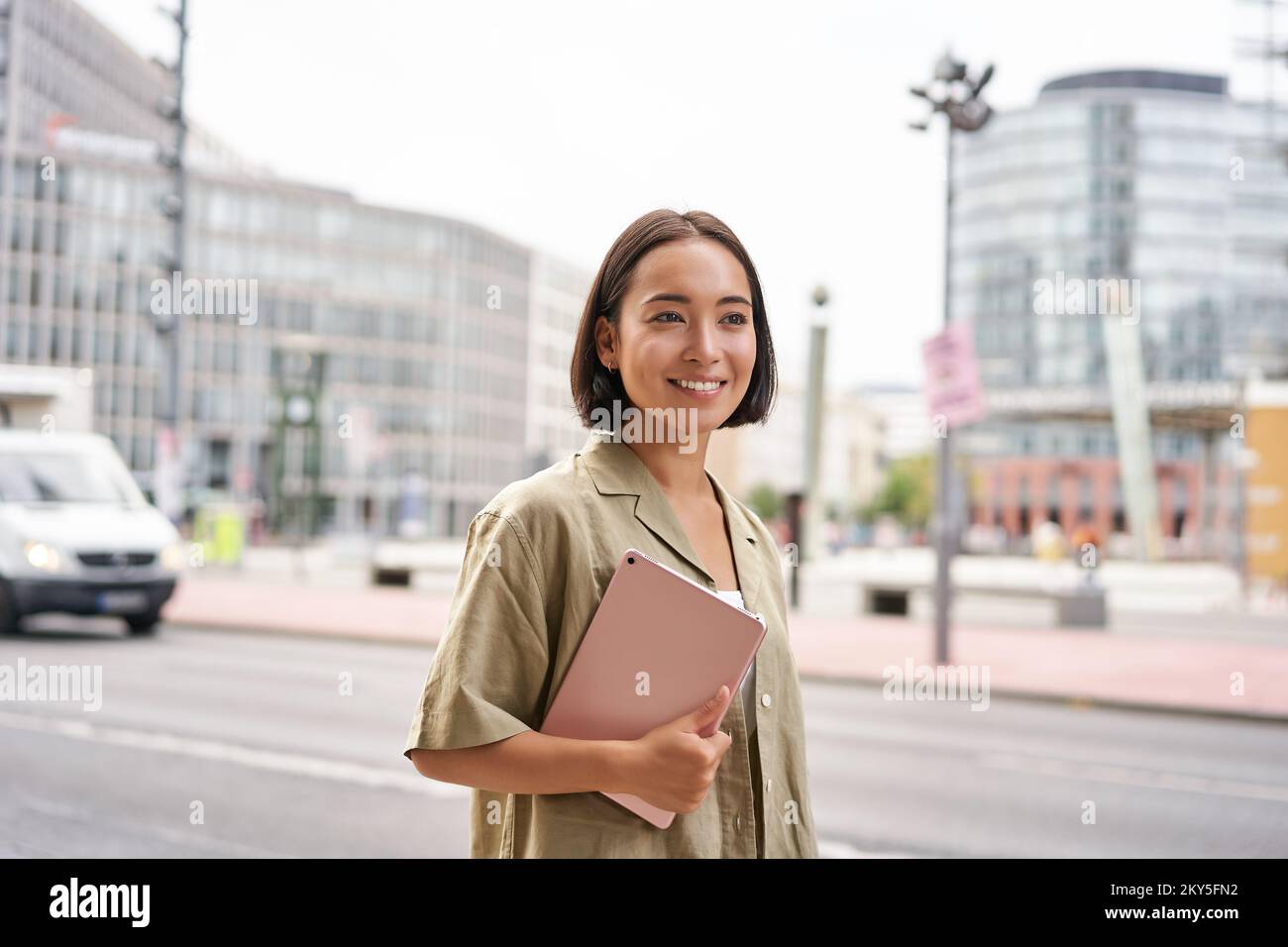 Portrait d'une jeune femme élégante marchant avec une tablette, se rendant quelque part en ville Banque D'Images