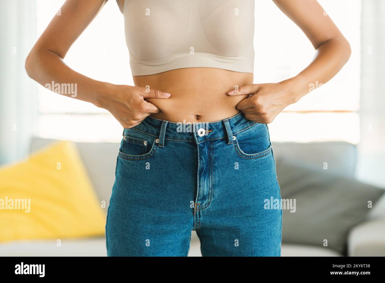 Jeune femme en jeans et blanc haut de la compression de sa graisse de ventre, la planification de la formation et de manger des aliments sains Banque D'Images