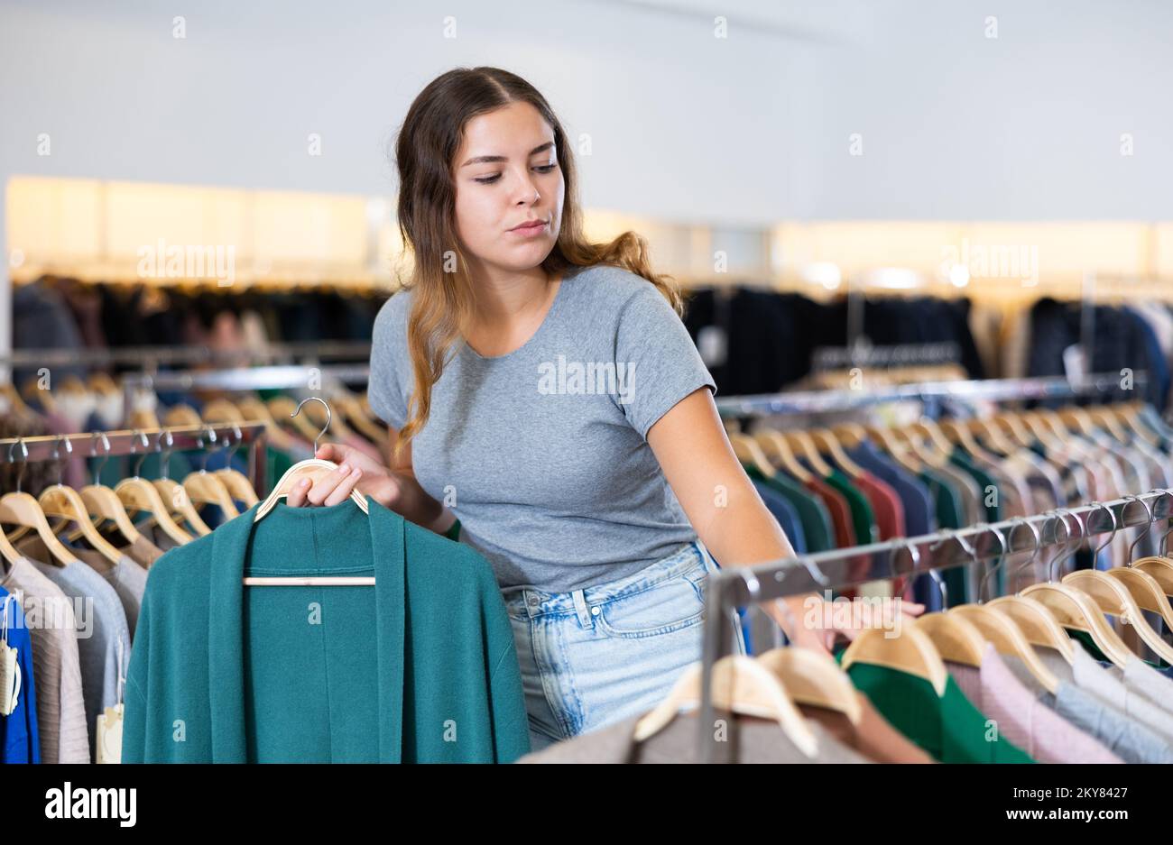 Jeune femme sérieuse tenant un gilet turquoise sur un rack tout en  choisissant des vêtements dans une boutique Photo Stock - Alamy