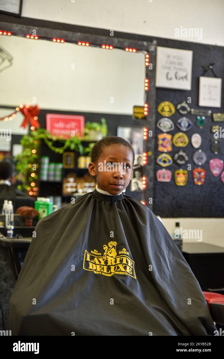 jeune garçon faisant un visage drôle en s'asseyant dans une chaise de barbershop en attendant que le barber coupe ses cheveux Banque D'Images