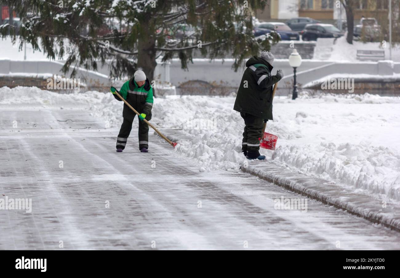 Les employés des services publics en uniforme nettoient le parc de la ville avec des pelles. Déneigement dans un parc hivernal Banque D'Images