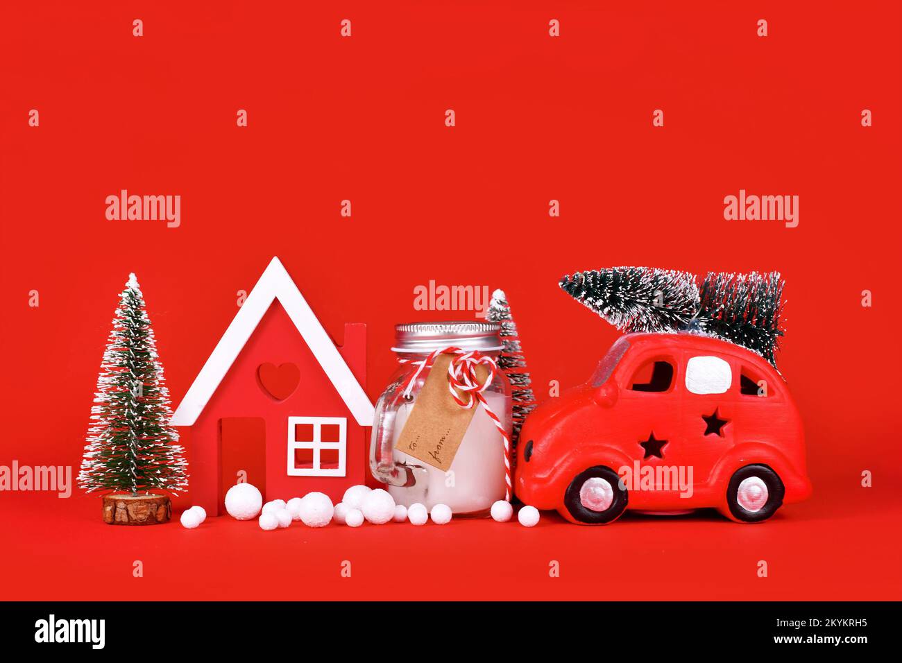 Décoration de Noël saisonnière avec voiture miniature, maison, arbres, bougie et boules de neige sur fond rouge Banque D'Images