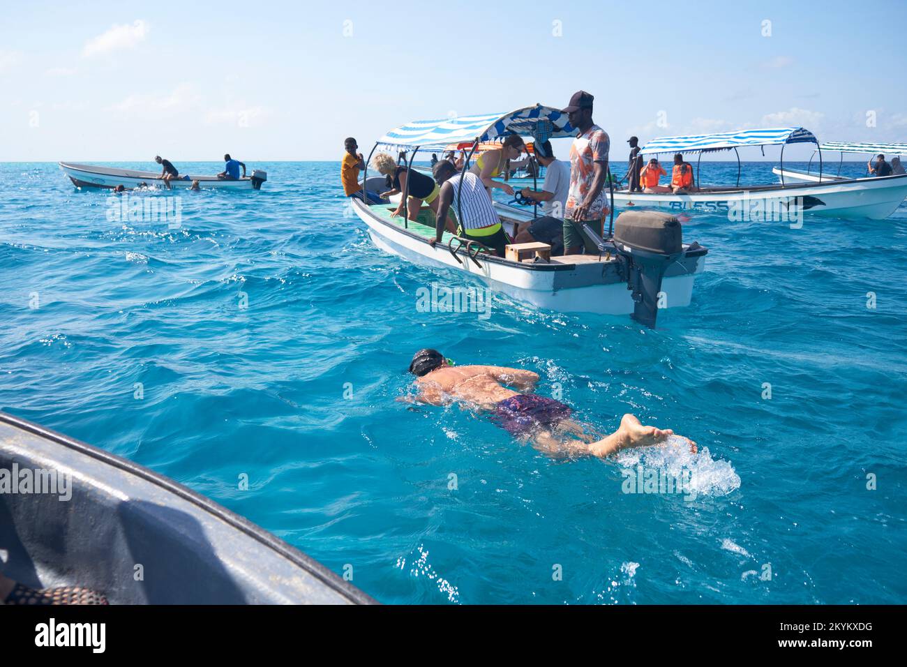 Les touristes sur la vue des dauphins voyant des excursions en bateau chasse les dauphins dans l'eau pour essayer de nager avec eux sur un site au large de la côte de l'atoll de Mnemba à Zanzibar, Banque D'Images