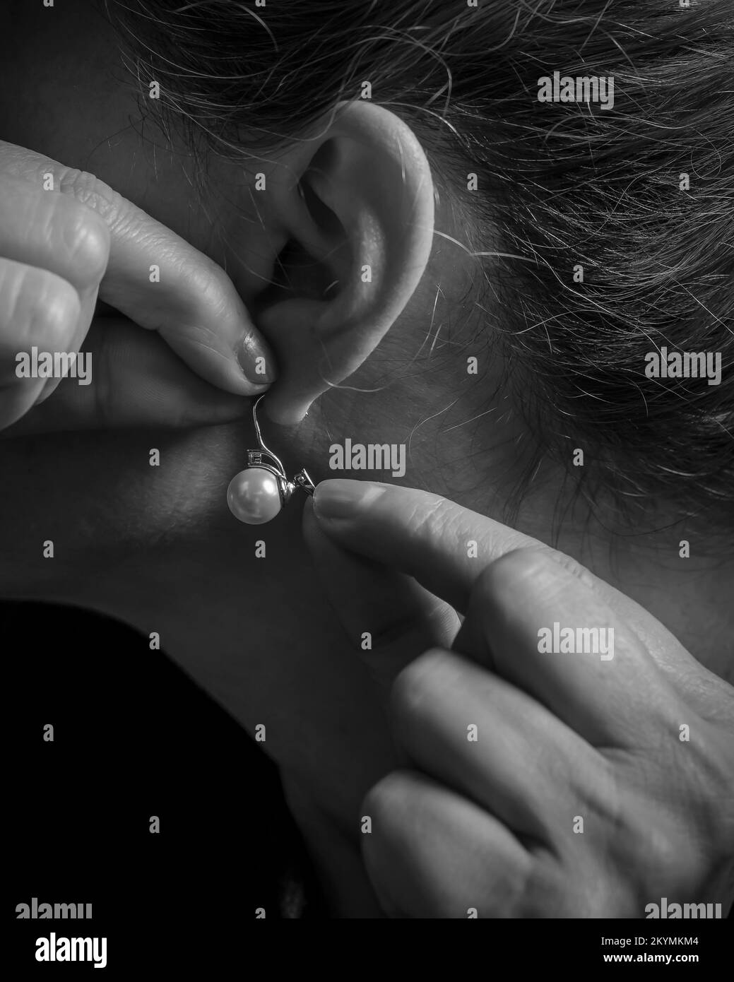 Vue rapprochée d'une femme mettant un contour d'oreille en perles, en noir et blanc Banque D'Images