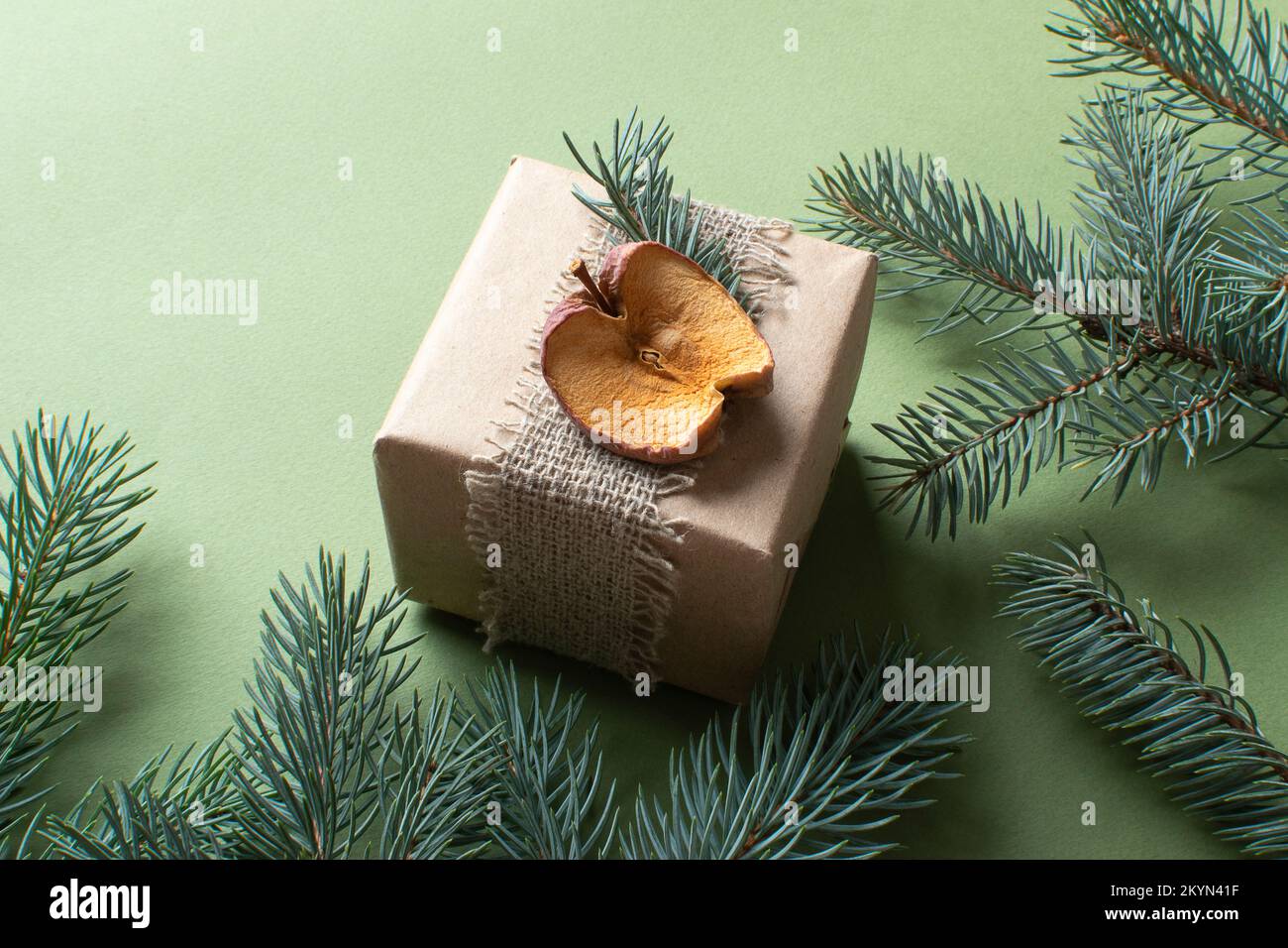 Un gros plan d'un cadeau de Noël enveloppé dans du papier kraft et peint avec des matériaux naturels, sur un fond vert, Noël zéro déchet . Faites-le vous-même Banque D'Images